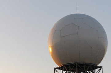 Close-up of a Doppler weather radar radome with hexagonal paneling, mounted on a metal tower, used for storm detection and atmospheric monitoring, reflecting sunlight against a clear sky in Arizona