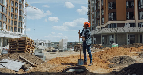 Middle aged builder in hard hat holding shovel on construction site