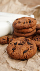 Cookies with chocolate drops on craft paper and bottles of milk. Vertical photo