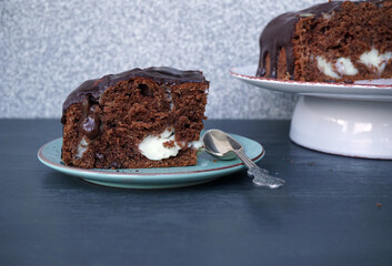 A piece of chocolate pie with white filling on a saucer and a pie on a stand in the background  