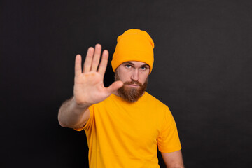 Portrait of bearded european man in yellow hat on black background serious look shows stop sign...