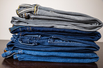 Folded jeans of various colors, arranged one on top of the other, and placed on a wooden surface.