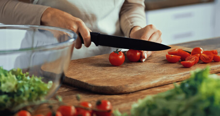 cropped view of woman cutting cherry tomatoes on chopping board