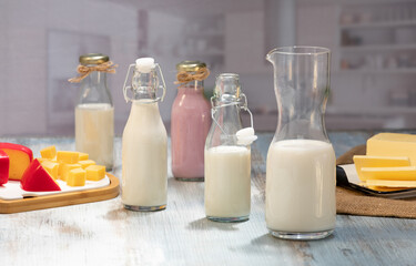 Bottles of milk and yogurt on a wooden table with cheese plater on a grey background