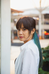 Portrait Asian woman in a white shirt with multicolor long hair, she is looking at a camera in front of a building background.