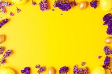 Easter yellow eggs with purple flowers on yellow background. Flat lay, copy space.