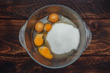 Eggs and yolk with sugar in a glass bowl on a brown wooden background top view, breakfast cooking concept, ingredients for making sponge dough and meringue, pancakes and pies