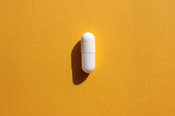 Single white pill on a colored yellow background. Hard light, shadow. Top view, copy space