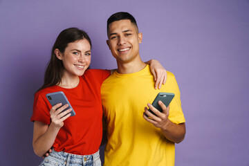 Happy beautiful couple hugging while using mobile phones