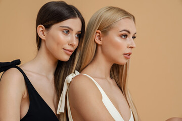 Sensual two women wearing swimsuits posing and looking aside