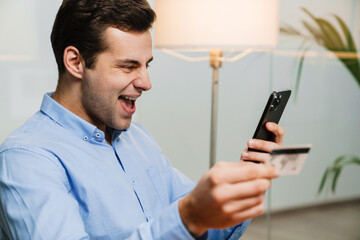 Happy office worker holding credit card and phone