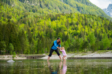 Fototapeta na wymiar Mother and daughter walking across forest lake.