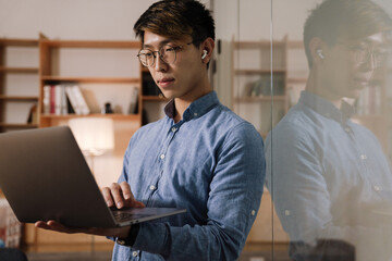 Obraz premium Focused asian guy in earphones working with laptop in office