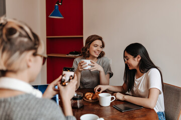 Selective focus of three girls with digital devices sitting at table. Good-humoured friends chilling during tea time.