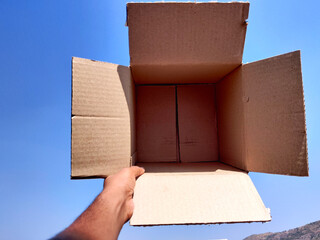 South Indian man hand holding empty brown box. Cloud background.
