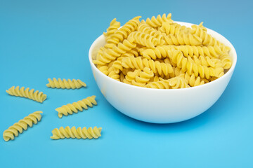 Fusilli italian pasta in white ceramical bowl on blue background.