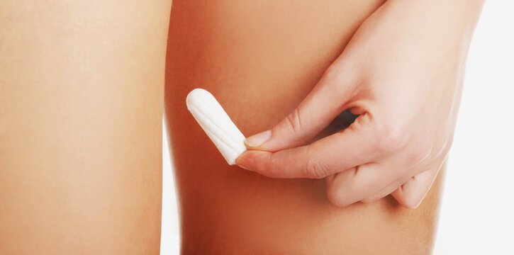 Woman legs and her hand holding vaginal cotton tampon. Menstruation sanitary and hygiene protection.