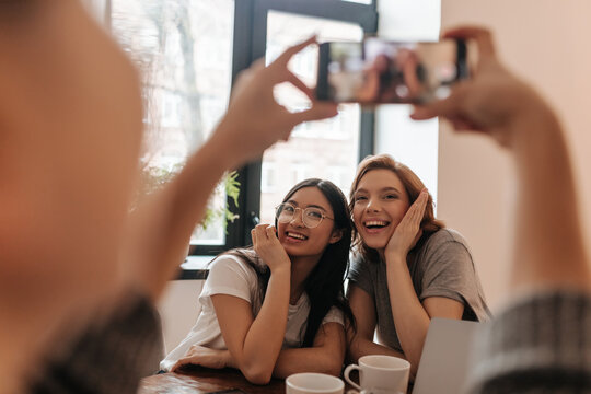Selective focus of woman with smartphone taking picture of smiling friends. Multicultural ladies posing while sitting at table.