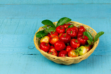 Acerola Cherry or Barbados Cherry with leaf in wicker basket on blue wooden background.