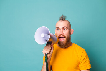 Bearded european man in yellow shirt isolated on turquoise background crazy shouting in megaphone loudspeaker, attention!