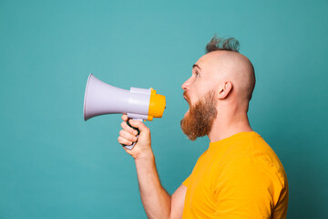 Bearded european man in yellow shirt isolated on turquoise background crazy shouting in megaphone...