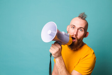 Bearded european man in yellow shirt isolated on turquoise background crazy shouting in megaphone loudspeaker, attention!