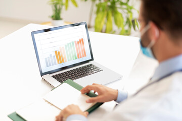 Male doctor analyzing datas while sitting at desk in doctor's office