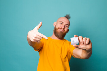 Bearded european man in yellow shirt isolated on turquoise background holding yes with surprise and...