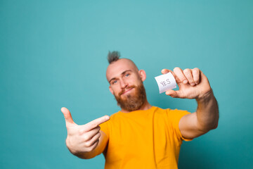 Bearded european man in yellow shirt isolated on turquoise background holding yes with surprise and...