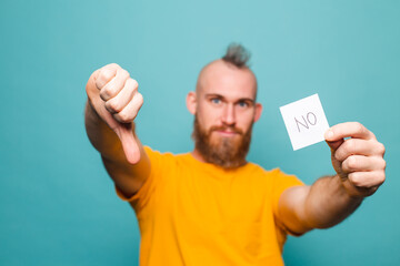 Bearded european man in yellow shirt isolated on turquoise background holding no strong man serious face
