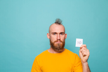 Bearded european man in yellow shirt isolated on turquoise background holding no strong man serious face