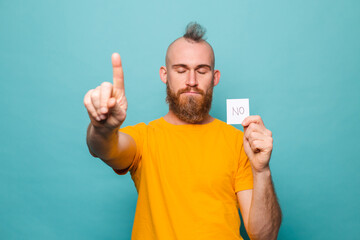 Bearded european man in yellow shirt isolated on turquoise background holding no strong man serious face