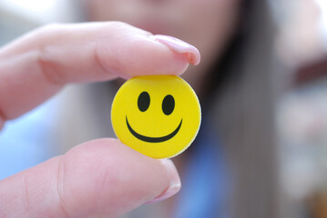 girl fingres holding yellow smiley sticker