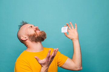 Bearded european man in yellow shirt isolated on turquoise background holding no screaming angry shocked