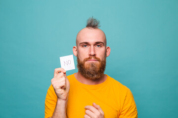 Bearded european man in yellow shirt isolated on turquoise background holding no strong man serious face