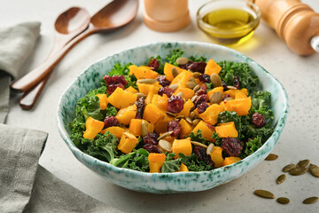 Fall salad with kale, roasted pumpkin, seeds and dried cranberries in bowl. Grey background. Mock up. Top view.