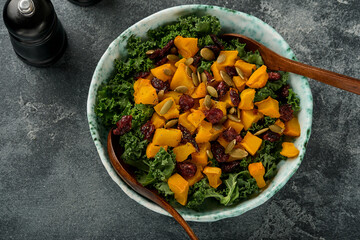 Fall salad with kale, roasted pumpkin, seeds and dried cranberries in bowl. Grey background. Mock up. Top view.