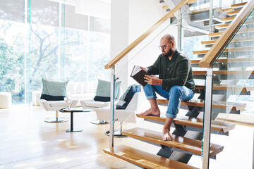 Bearded man spending time with book in penthouse apartment