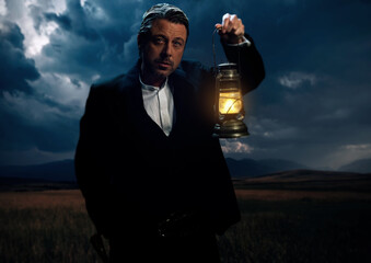 Man in victorian clothing with lantern standing on prairie area.