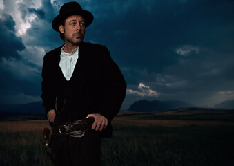 Man in victorian cowboy clothing with revolver in holster standing on prairie area.