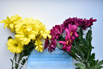 Blue medical face mask and the colorful spring bouquets of yellow and purple daisies.