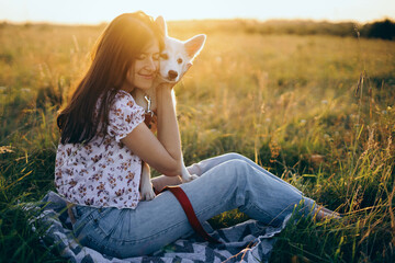Happy woman cuddling with cute white puppy in summer meadow in  sunset. Happiness. Summer vacation