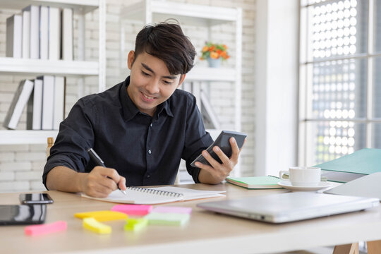 An Asian Young Business Man Work From Home, Using The Calculator To Calculator His Financial Status