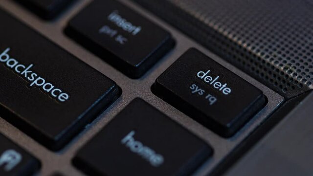A human finger is pressing the Delete key on the black computer keyboard.