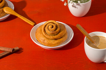 Freshly baked cinnamon bun stuffed with spices and cocoa on a red table with a hard shadow. Sweet homemade cakes.