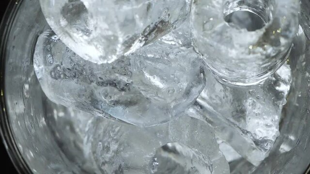 Ice cubes drop into tall clear glass and fill to top. Look down close up view of glass being filled with ice to prepare drink for service. Beverage preparation.