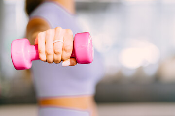 Cropped body close up of young unrecognizable woman in sport clothes holding weight pink dumbbell...