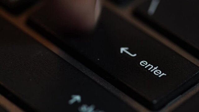 A human finger is pressing the Enter key on the black computer keyboard.