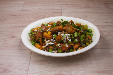 Paneer Chilis is an Indian dish, paneer cubes with tomatoes, onions, spring onions, chilli sauce. served on rustic wooden background, selective focus