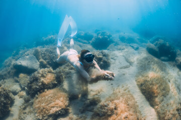 Woman glides with sand in hand. Free diver with fins posing underwater